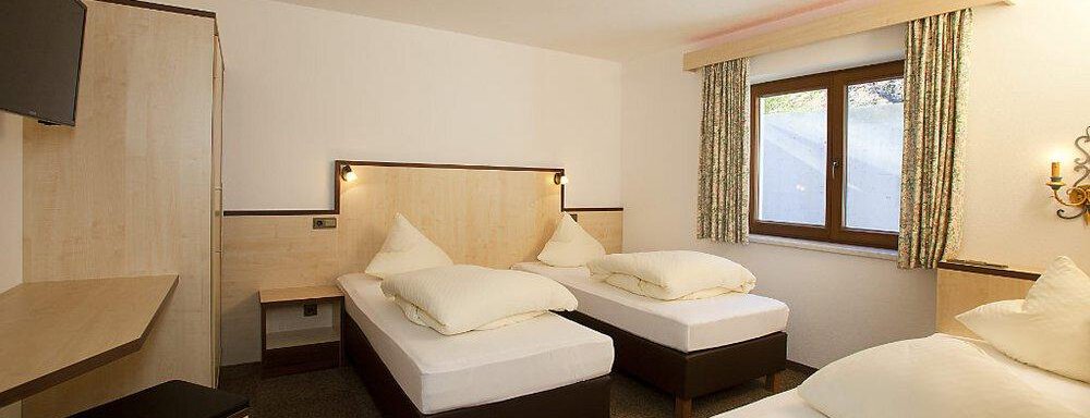 A cozy bedroom with three single beds and simple furniture. The room has large windows and a modern touch. - Appartement Alpin - Sölden