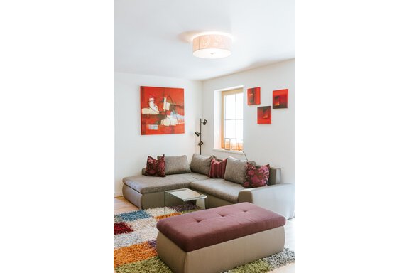 A modern living room with a gray couch and colorful cushions. Abstract paintings hang on the wall, and the floor is covered with a colorful rug. - Appartement Bergbach Sölden - Sölden