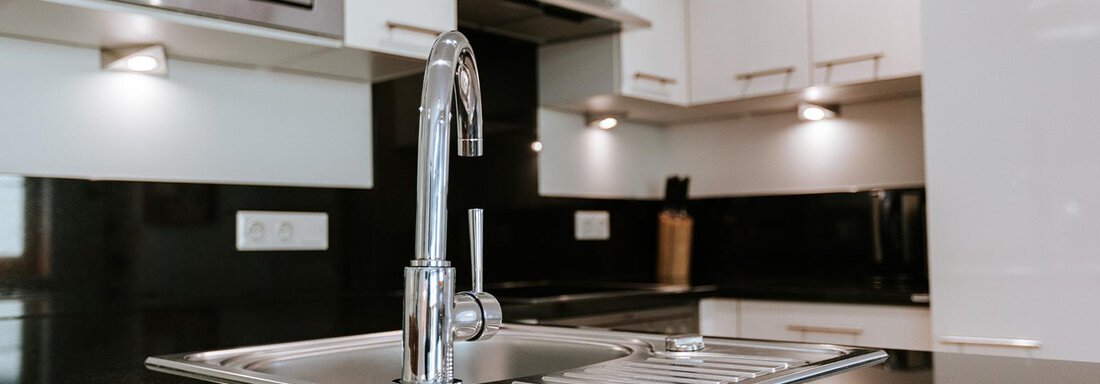 A modern kitchen with a shiny black countertop. The sink and the mixer are centrally located, surrounded by stylish kitchen cabinets. - Appartement Bergbach Sölden - Sölden