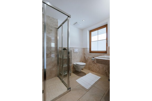 A modern bathroom with a glass shower and a light color palette. The space is well-lit and features a large window front. - Appartement Bergbach Sölden - Sölden