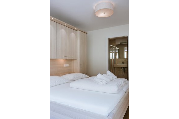 A modern bedroom with a two persons bed. In the background, a bathroom is visible. - Appartement Bergbach Sölden - Sölden