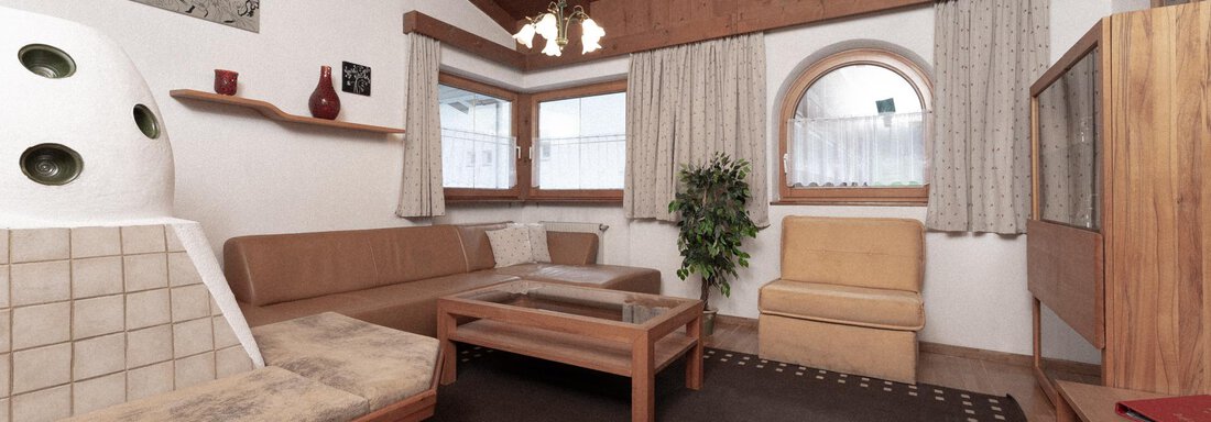 A cozy living room with wooden ceilings and large windows. The furniture is simple and welcoming, with a rug in the center. - Appartement Gehörde Sölden - Sölden