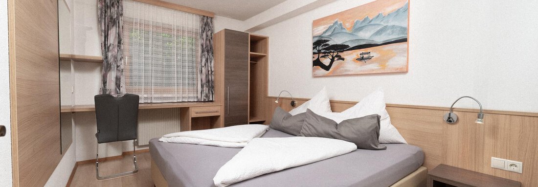 A cozy room with a large bed and a desk. A beautiful landscape painting hangs on the wall. - Appartement Gehörde Sölden - Sölden