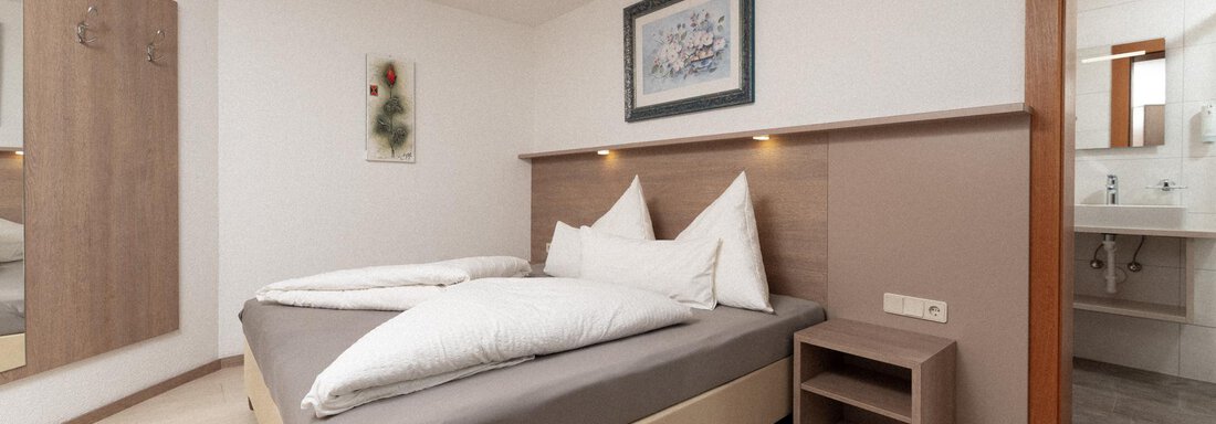 A modern bedroom with a double bed and light wood interior. The walls are in neutral colors, and a bathroom is visible. - Appartement Gehörde Sölden - Sölden