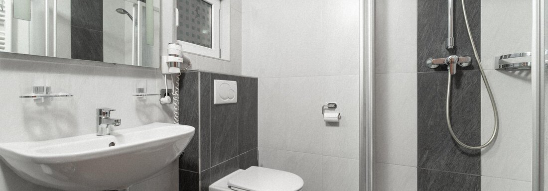 A modern bathroom with a shower, sink, and toilet. The walls are tiled in light colors, and there are large mirrors. - Appartement Gehörde Sölden - Sölden