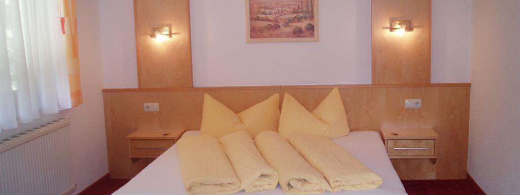 A simple room with a large bed and yellow pillows. The walls are bright, and there is a red carpet. - Appartement Harmonie - Sölden