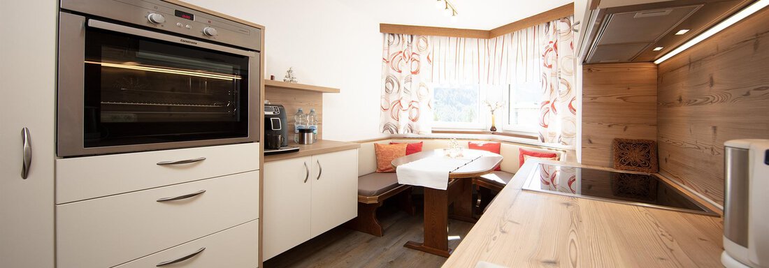 Kueche A modern kitchen with white furniture and wood details. The space is bright and inviting, with a table and a cozy seating area. - Appartement Harmonie - Sölden