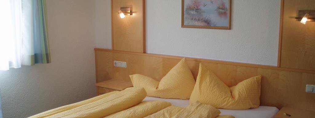 A cozy bedroom with a large bed and yellow blankets. The walls are light, and there is a picture above the bed. - Appartement Harmonie - Sölden