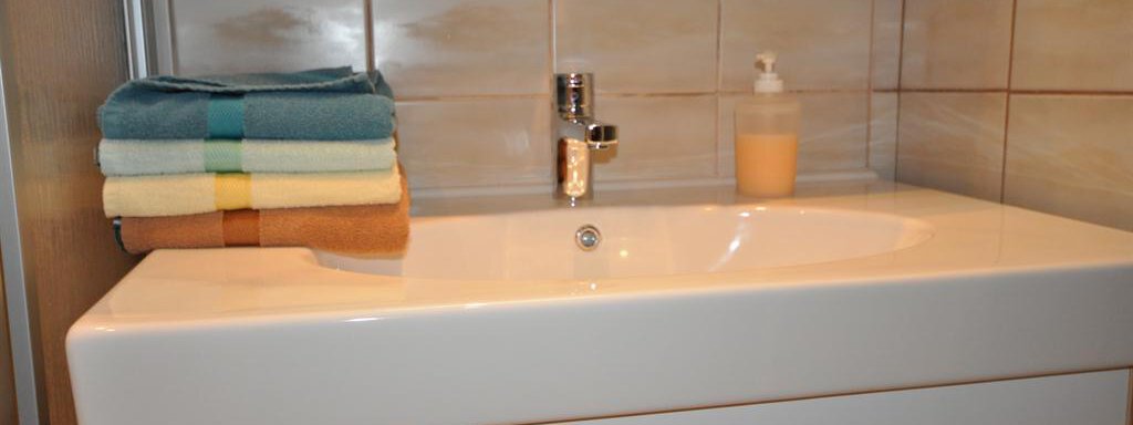 A modern sink with clean towels in various colors. Tiles are visible in the background. - Appartement Harmonie - Sölden