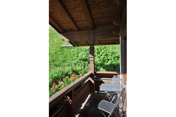 A cozy balcony with a wooden railing and two chairs. In the background, blooming plants and lush greenery. - Appartement Harmonie - Sölden