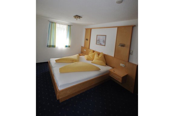A cozy bedroom with a large bed and yellow pillows. The walls are bright, and the windows let in plenty of light. - Appartement Harmonie - Sölden