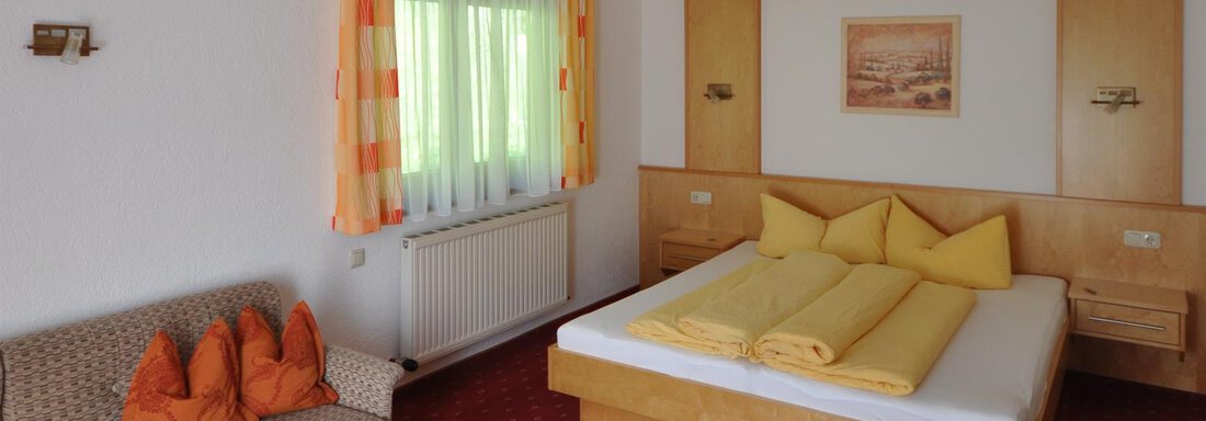 A bright room with a double bed and several yellow cushions. There is a cozy seating area with a sofa and a small table. - Appartement Harmonie - Sölden