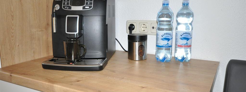 A coffee machine is on a wooden tray next to two bottles of water. Next to it is a cup. - Appartement Harmonie - Sölden