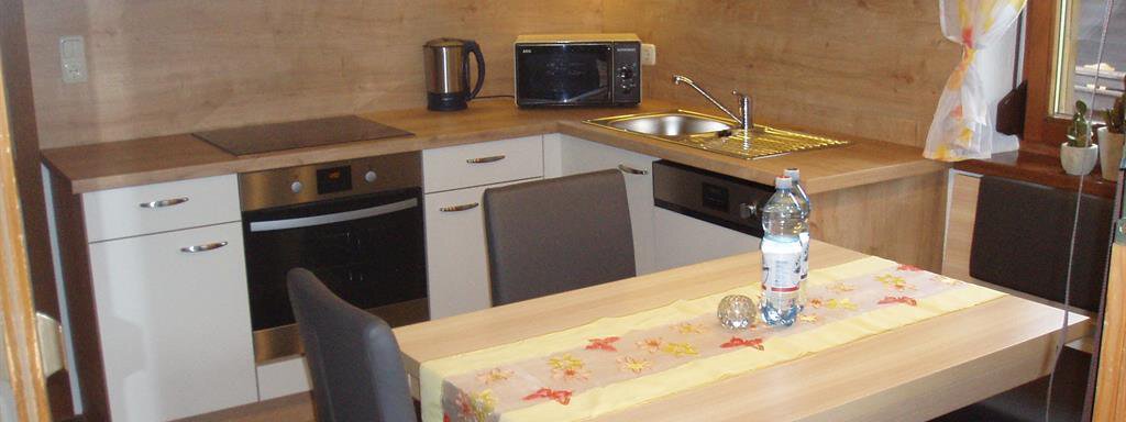A modern kitchen with wooden shelves and white cabinets. On the table are a water bottle and decorative table setting. - Appartement Harmonie - Sölden