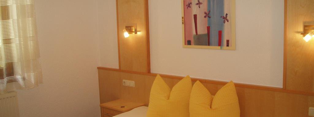 A cozy bedroom with a large double bed and yellow pillows. A colorful picture hangs on the wall and there is soft light from the wall lamps. - Appartement Harmonie - Sölden