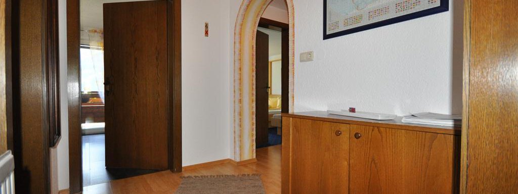 A hallway with wooden flooring and a light wall. In the background, doors and a world map on the wall can be seen. - Appartement Harmonie - Sölden