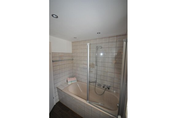 A modern bathroom with a bathtub and a shower partition. The walls are tiled and there are soft towels. - Appartement Harmonie - Sölden