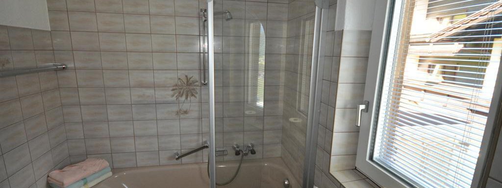 A modern bathroom with a bathtub and a shower. It has bright tiles and a window that lets in natural light. - Appartement Harmonie - Sölden