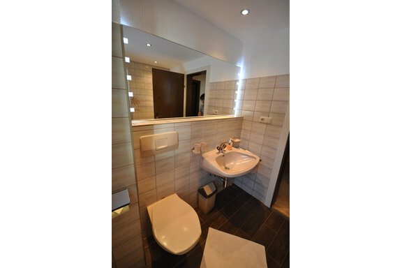 A modern bathroom with bright tiles and a large mirror. It is equipped with a sink, a toilet, and a small trash can. - Appartement Harmonie - Sölden