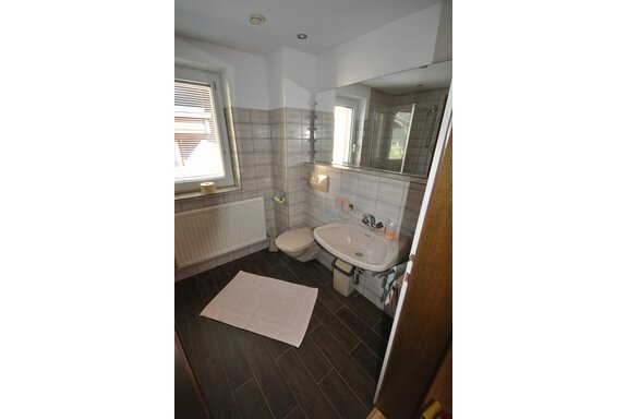 A modern bathroom with a sink and a toilet. The floor is tiled with dark tiles and there is a large window. - Appartement Harmonie - Sölden