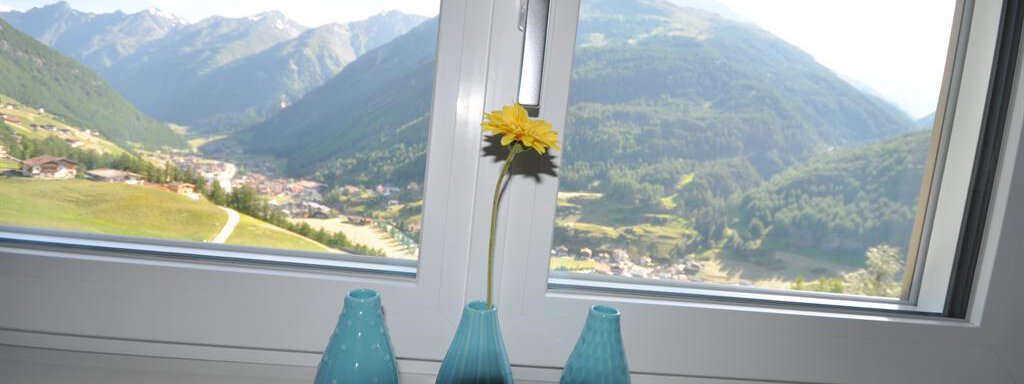 A windowsill with three blue vases and a flower in the middle. In the background, mountains and a green landscape can be seen. - Appartement Harmonie - Sölden