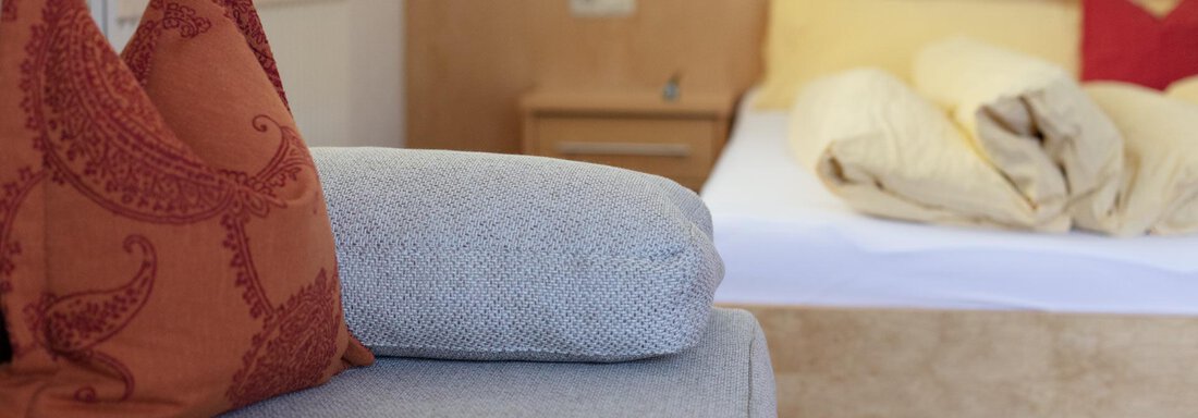 A cozy bedroom with an unmade bed and decorative pillows on a couch. The warm colors create an inviting atmosphere. - Appartement Harmonie - Sölden
