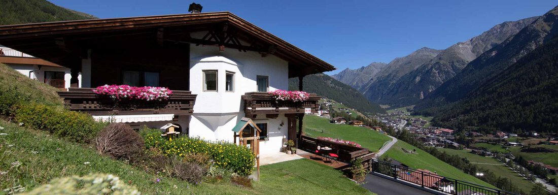 A cozy house in the mountains with blooming flowers on the balcony. In the background, green meadows and majestic mountains stretch out. - Appartement Harmonie - Sölden