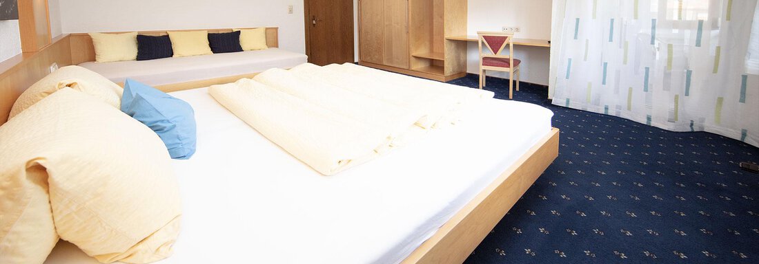 A modern bedroom with a large bed and a cozy seating area. The room is bright and friendly designed, with a blue carpet and window curtains. - Appartement Harmonie - Sölden