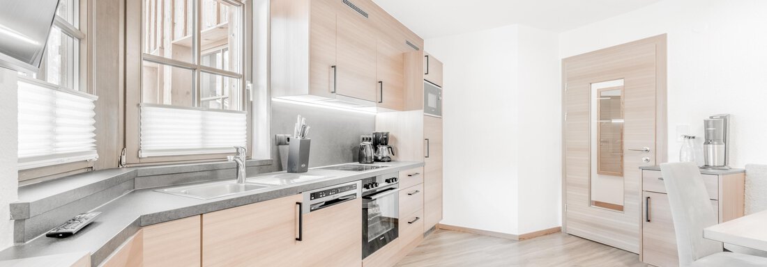 A modern kitchen with wood-colored cabinets and a bright, inviting atmosphere. The countertop is made of gray stone, and there is a separate door to the adjacent room. - Appartement Montanara - Sölden