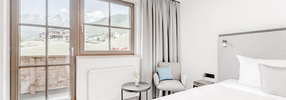 A modern bedroom with a large window and a view of the mountains. The room is bright and furnished in a minimalist style. - Appartement Montanara - Sölden