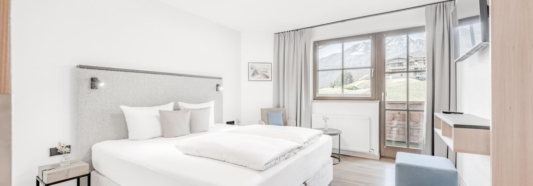 A modern bedroom with a large bed and bright walls. Large windows offer a view of the outside and let in plenty of daylight. - Appartement Montanara - Sölden