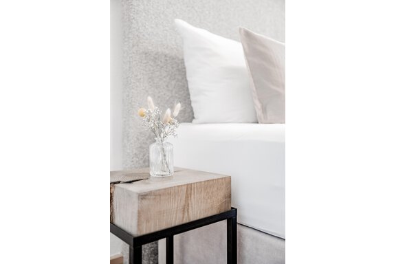 A cozy bedroom with a bed and a wooden table. On the table is a small vase with dried flowers. - Appartement Montanara - Sölden