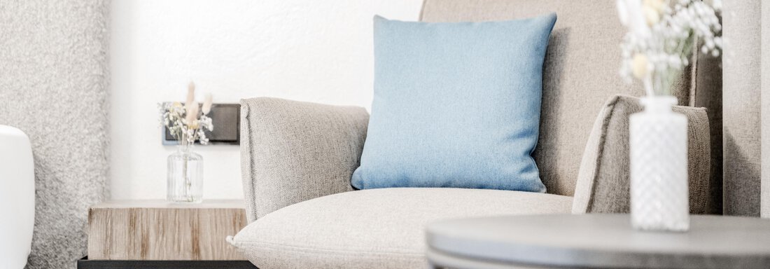 A cozy armchair with a blue cushion is next to a small table. On the table, there is a vase with flowers. - Appartement Montanara - Sölden