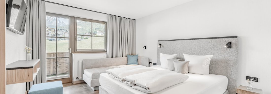 A modern hotel room with a large double bed and a comfortable seating area. Light streams through the windows, creating a bright, inviting atmosphere. - Appartement Montanara - Sölden