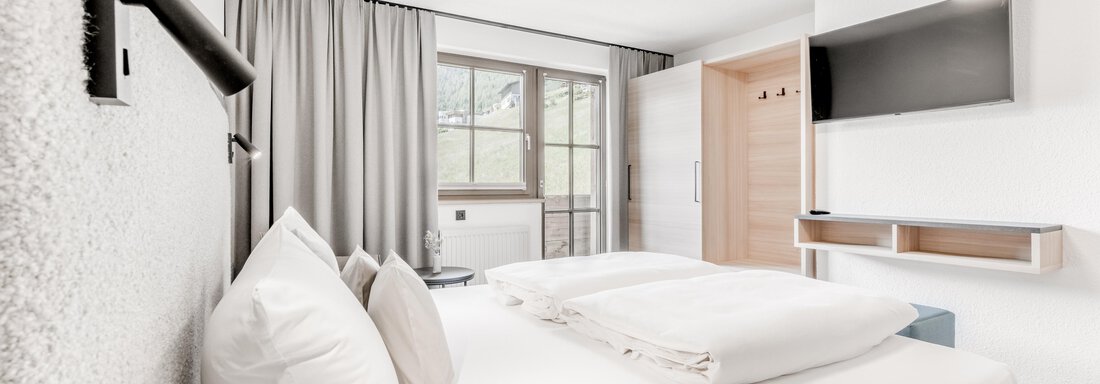 A modern bedroom with a large bed and bright walls. There is a television and a window that lets in a lot of light. - Appartement Montanara - Sölden