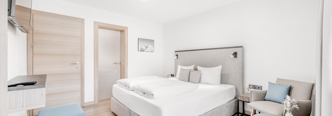 A modern bedroom with a large double bed and stylish furniture. The room is bright and designed in a minimalistic style. - Appartement Montanara - Sölden