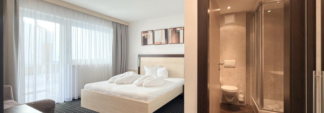 A modern hotel room with a large bed and two pillows. The room has its own bathroom area and large windows that let in plenty of light. - Appartementhaus A CASA "Kristall" - Sölden