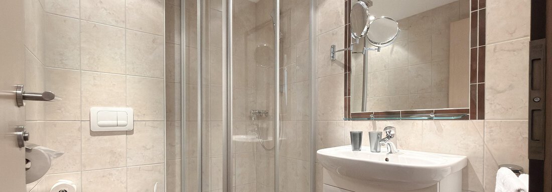 A modern bathroom with a glass shower and a sink. The walls are decorated with light tiles and there is a toilet. - Appartementhaus A CASA "Kristall" - Sölden