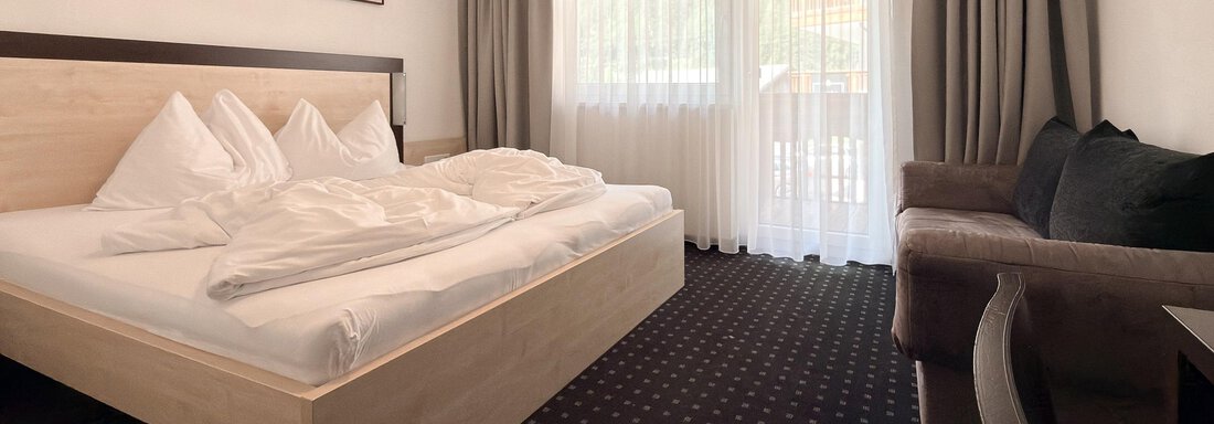 A modern hotel room with a large bed and a comfortable couch. 

Large windows provide plenty of natural light and a pleasant stay. - Appartementhaus A CASA "Kristall" - Sölden