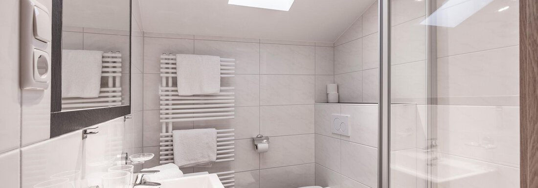 A modern bathroom with a shower, a sink, and a toilet. The room has bright tiles and plenty of daylight through a skylight. - Appartementhaus Fender - Sölden