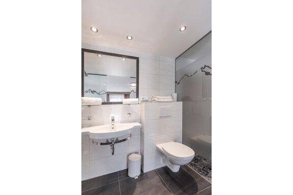 A modern bathroom with a glass shower and a toilet area. The walls are brightly tiled, and there are fresh towels on a shelf. - Appartementhaus Fender - Sölden