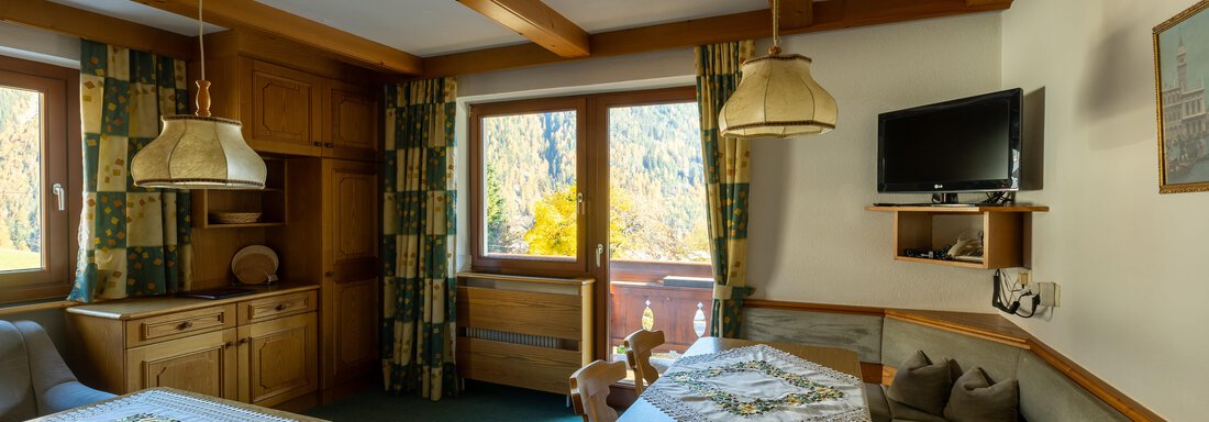 A cozy living space with wooden furniture and a view of nature. Large windows provide plenty of daylight and create an inviting atmosphere. - Appartementhaus Karlinger - Sölden