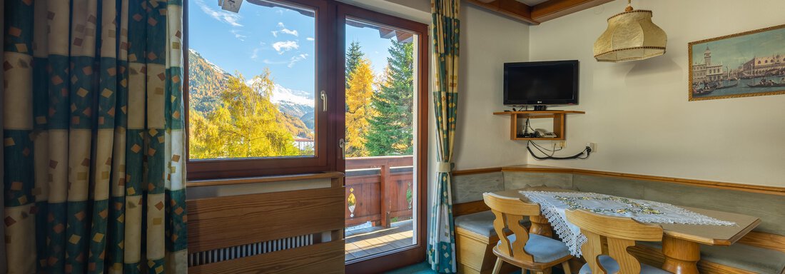 A cozy living space with large windows and a beautiful view of the mountains. The room is equipped with a table and chairs as well as a television. - Appartementhaus Karlinger - Sölden