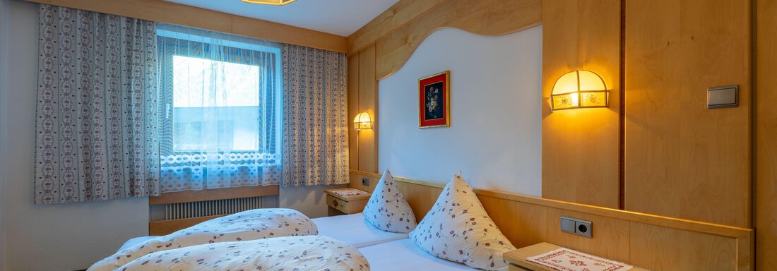 A cozy bedroom with a double bed and decorative pillows. The room is bright and friendly, with windows and wooden paneling. - Appartementhaus Karlinger - Sölden