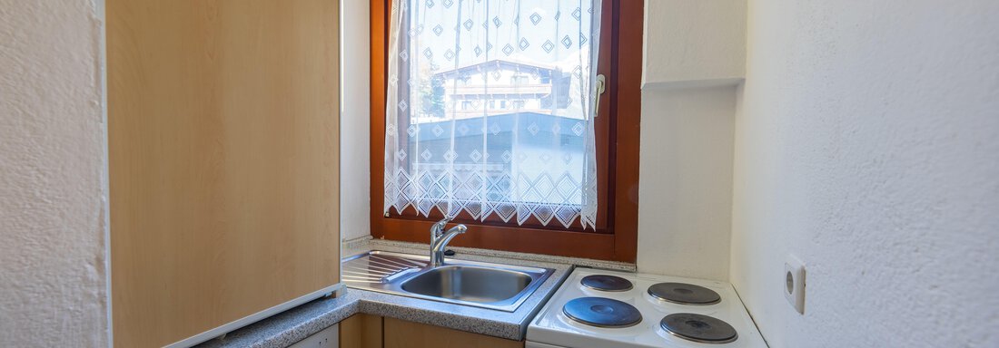 A small, modern kitchen with wooden cabinets and a window. It is equipped with a sink, a stove, and a microwave. - Appartementhaus Karlinger - Sölden