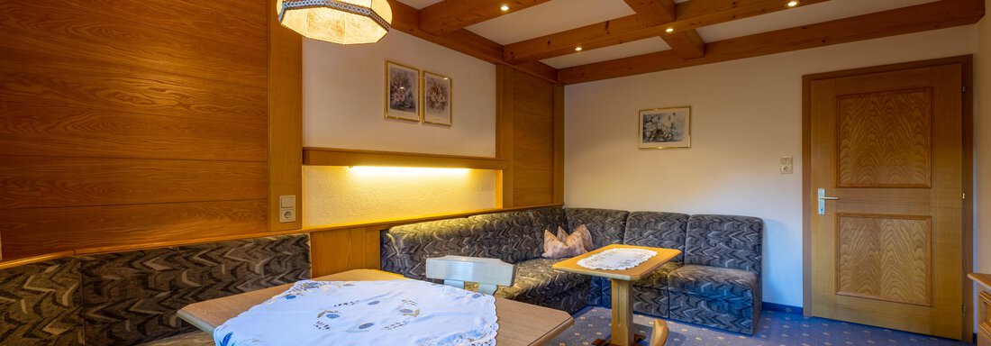 A cozy living area with wood paneling and an inviting seating area. A table and chairs complement the warm, friendly atmosphere. - Appartementhaus Karlinger - Sölden