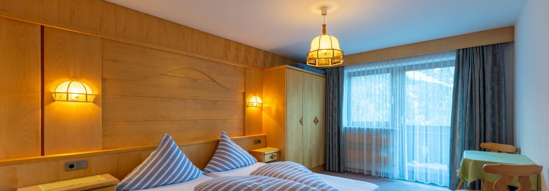 A cozy bedroom with a double bed and blue pillows. Large windows provide daylight and access to a balcony. - Appartementhaus Karlinger - Sölden