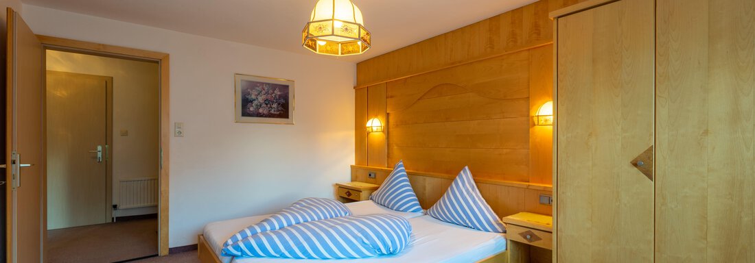 A cozy bedroom with a double bed and two pillows. The room is designed in warm wooden tones and has an inviting atmosphere. - Appartementhaus Karlinger - Sölden