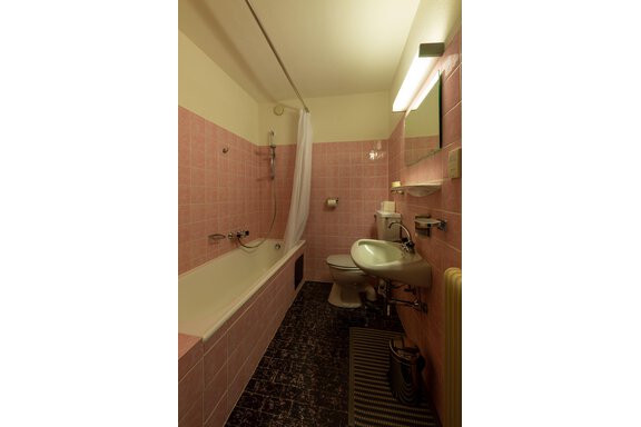 A bathroom with pink tiles and a bathtub. There is a sink, a toilet, and a mirror. - Appartementhaus Karlinger - Sölden