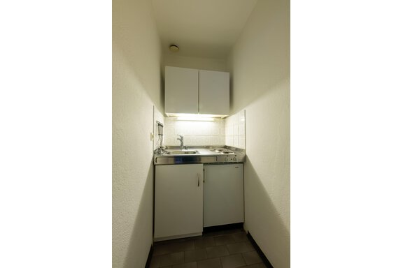A small, modern kitchen with white cabinets and a sink. The walls are bright and the lighting is warm. - Appartementhaus Karlinger - Sölden